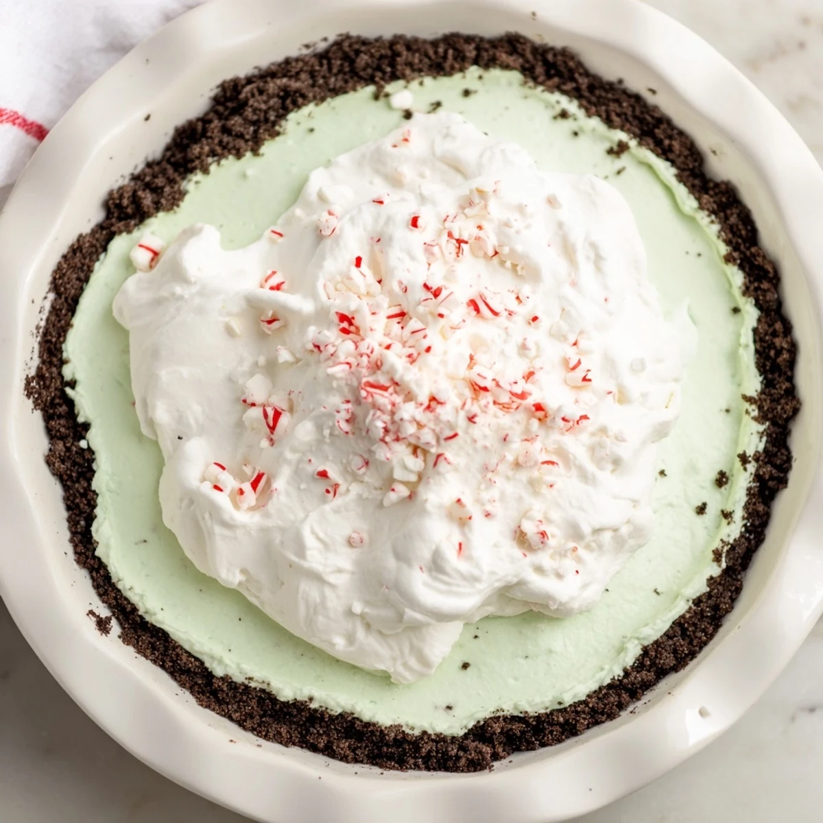 A luscious slice of Peppermint Cream Pie with fluffy whipped cream and crushed peppermint candies.