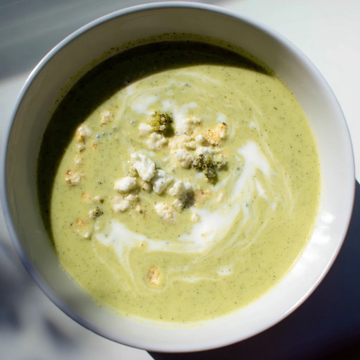 A bowl of Creamy Broccoli and Stilton Soup, with a swirl of cream, inviting you to enjoy its rich flavors.