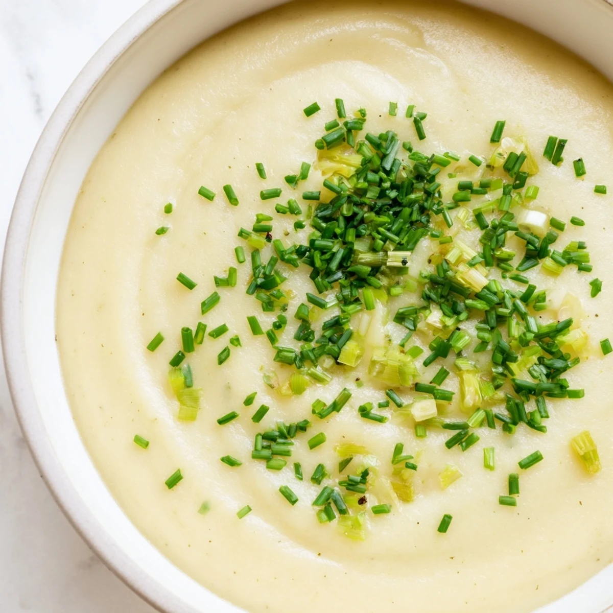 A close-up view of velvety creamy potato leek soup swirled with fresh herb garnish.