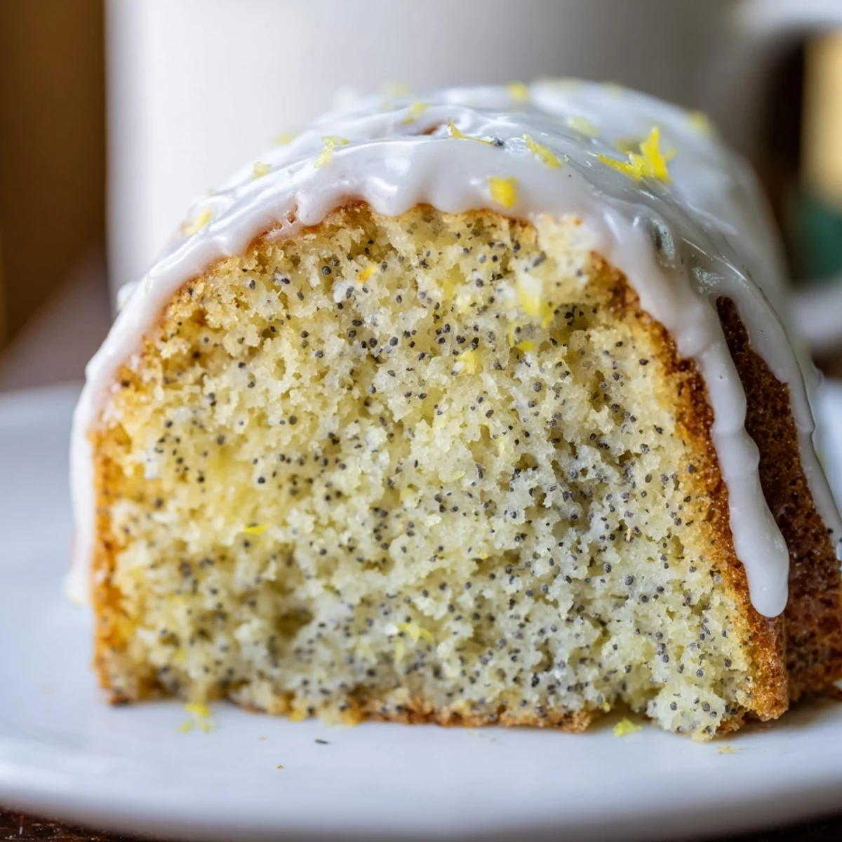 Glazed Lemon Poppy Seed Bundt Cake drizzled on a wire rack with fresh lemon slices and tea nearby.