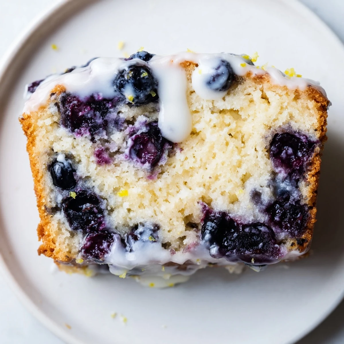 Freshly baked Lemon and Blueberry Yogurt Loaf with a golden crust, moist crumb, and bright lemon glaze dripping down the sides.