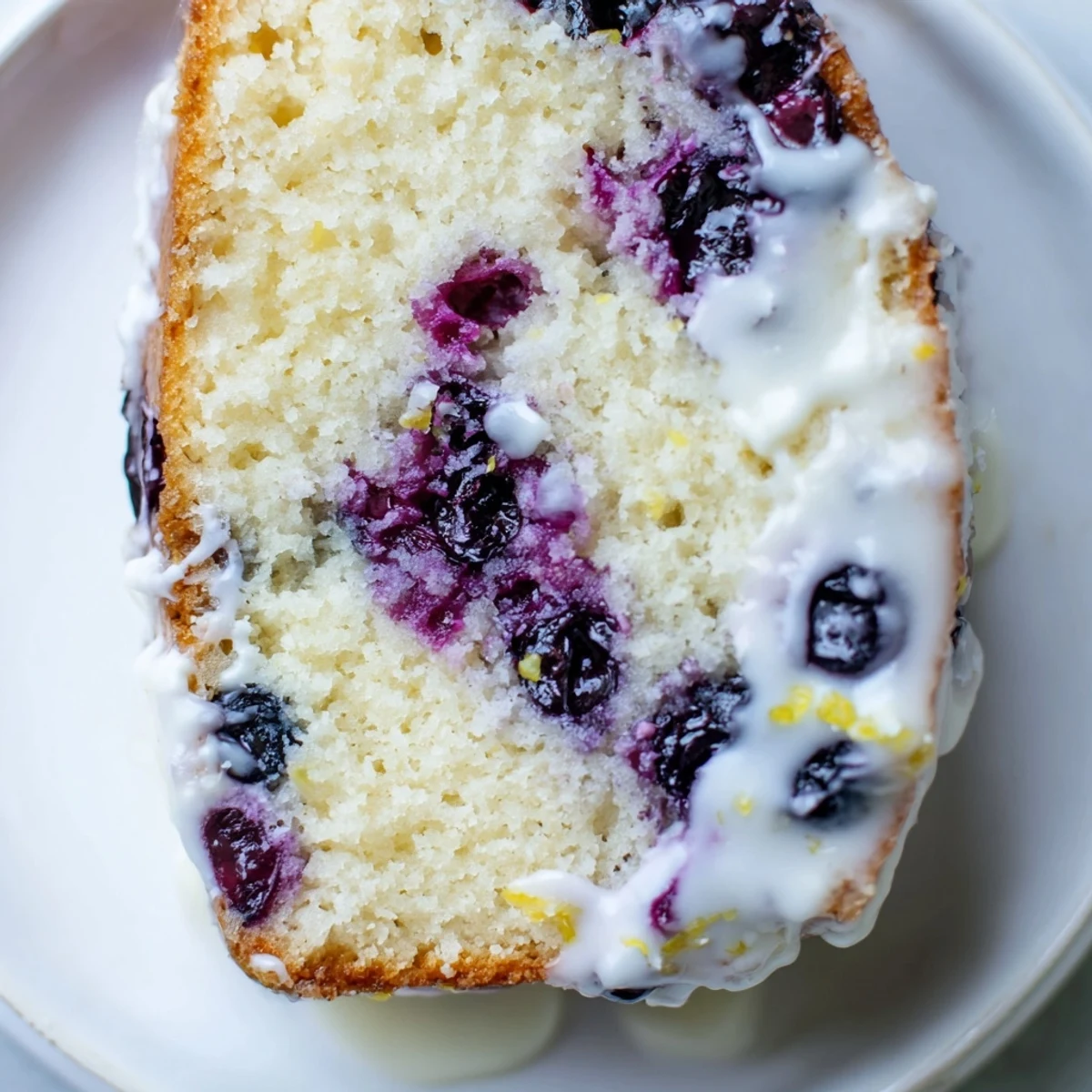Slice of Lemon and Blueberry Yogurt Loaf on a plate, topped with fresh blueberries and a dollop of whipped cream.
