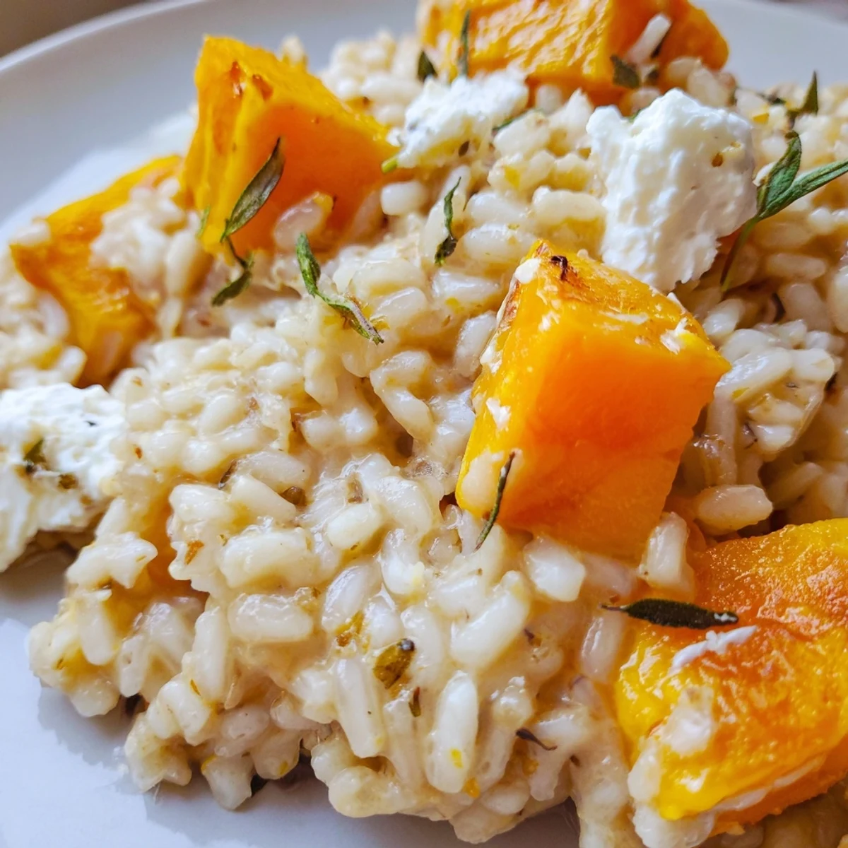 A comforting bowl of Butternut Squash and Goat Cheese Risotto topped with extra tangy goat cheese crumbles and a drizzle of olive oil, served warm.