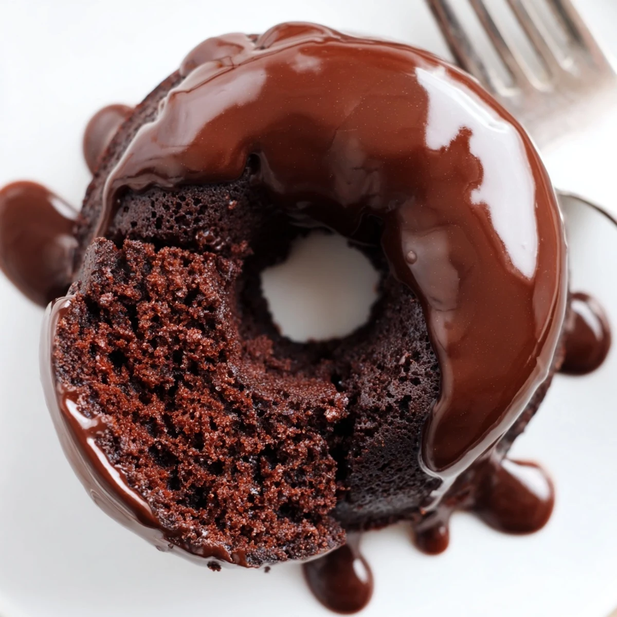 A warm chocolate donut with glaze drizzle beside a glass of cold milk for dunking.