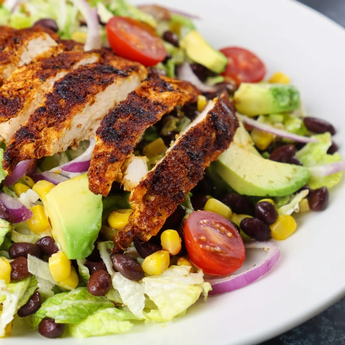 Southwest Chicken Salad is served in a large glass bowl, showcasing creamy avocado wedges, vibrant red onion rings, and fresh cilantro sprinkled on top for a colorful lunch.