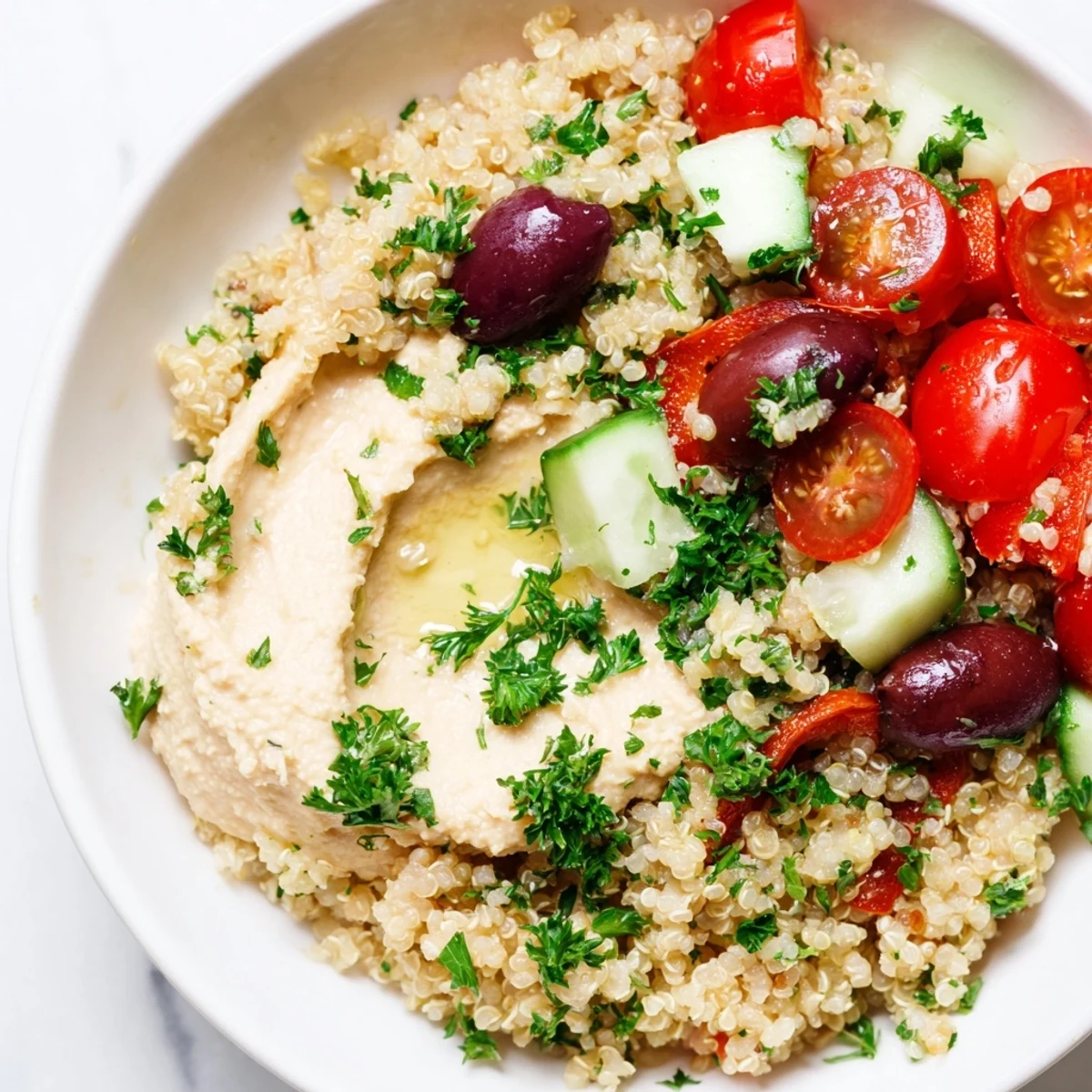 Freshly cooked quinoa forms the base of a vibrant Mediterranean Quinoa Bowl topped with crisp cucumber, tomatoes, and a creamy dollop of hummus.