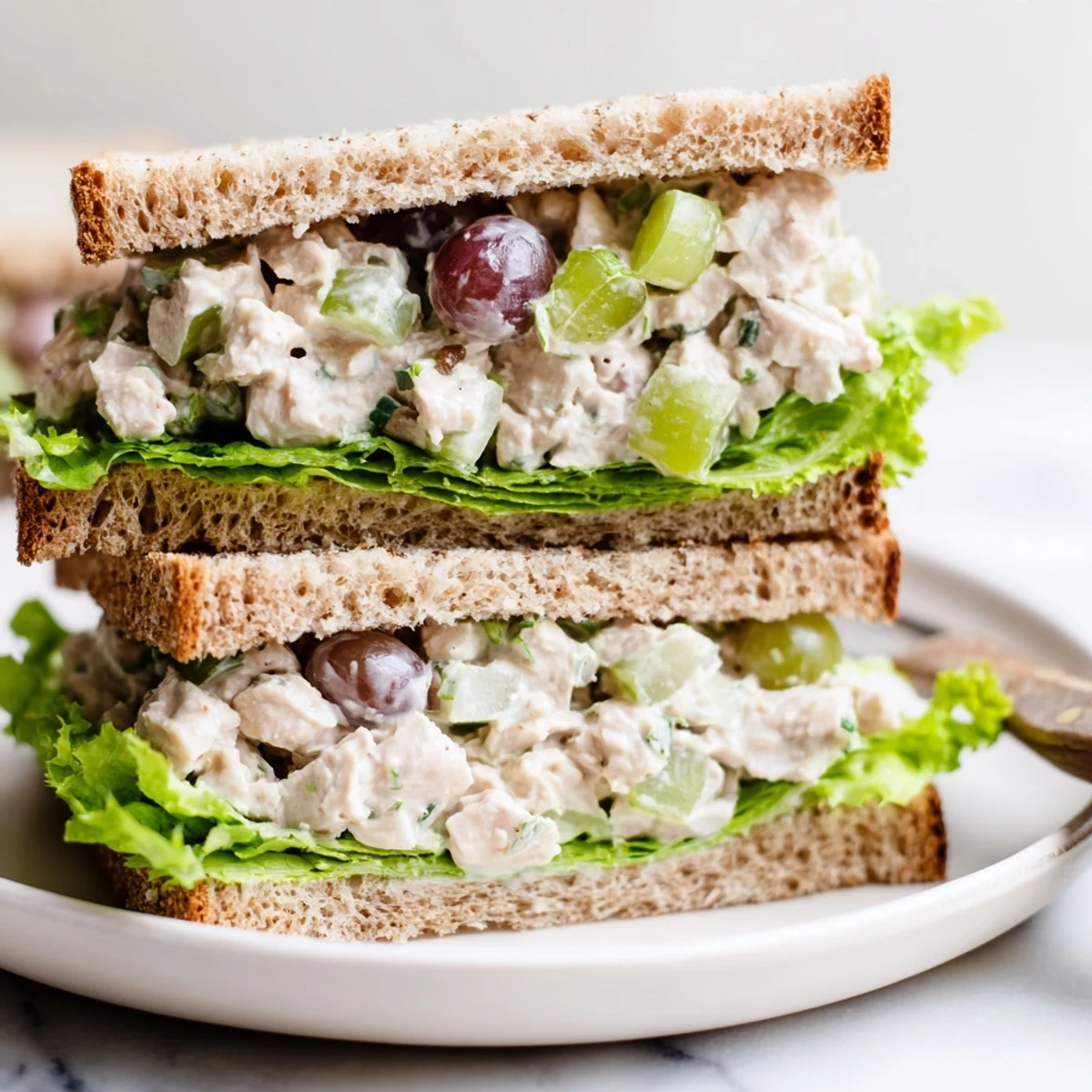 A close-up of a Chicken Salad Sandwich with Grapes, featuring tender chicken, halved grapes, and crunchy celery in a creamy dressing on toasted bread.