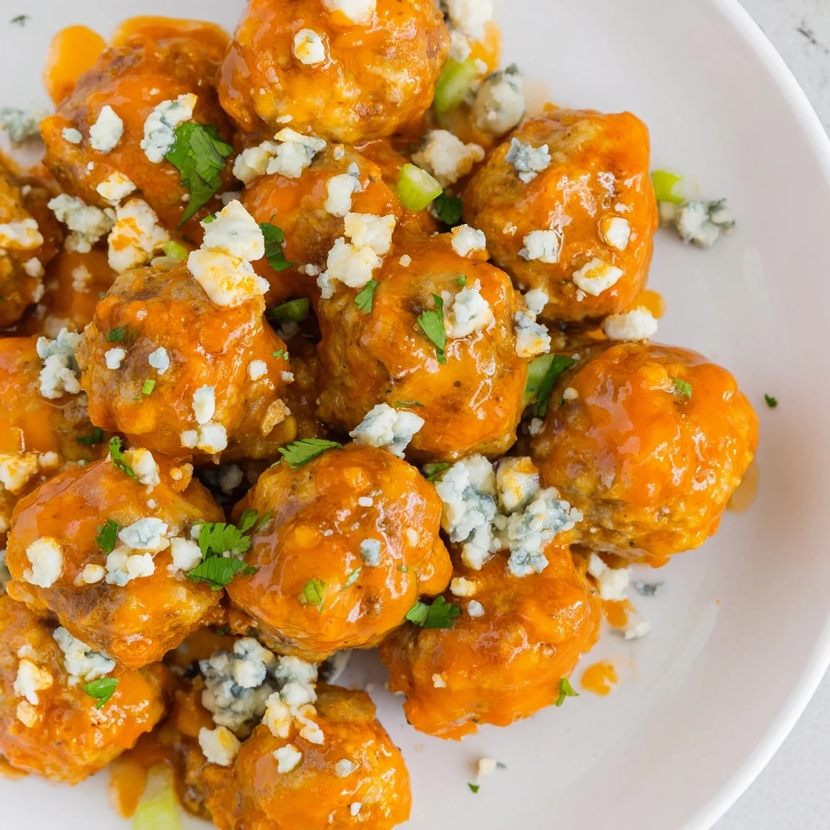 Game Day Spicy Buffalo Chicken Meatballs glazed in a zesty orange-red sauce, served on a platter with fresh celery sticks.