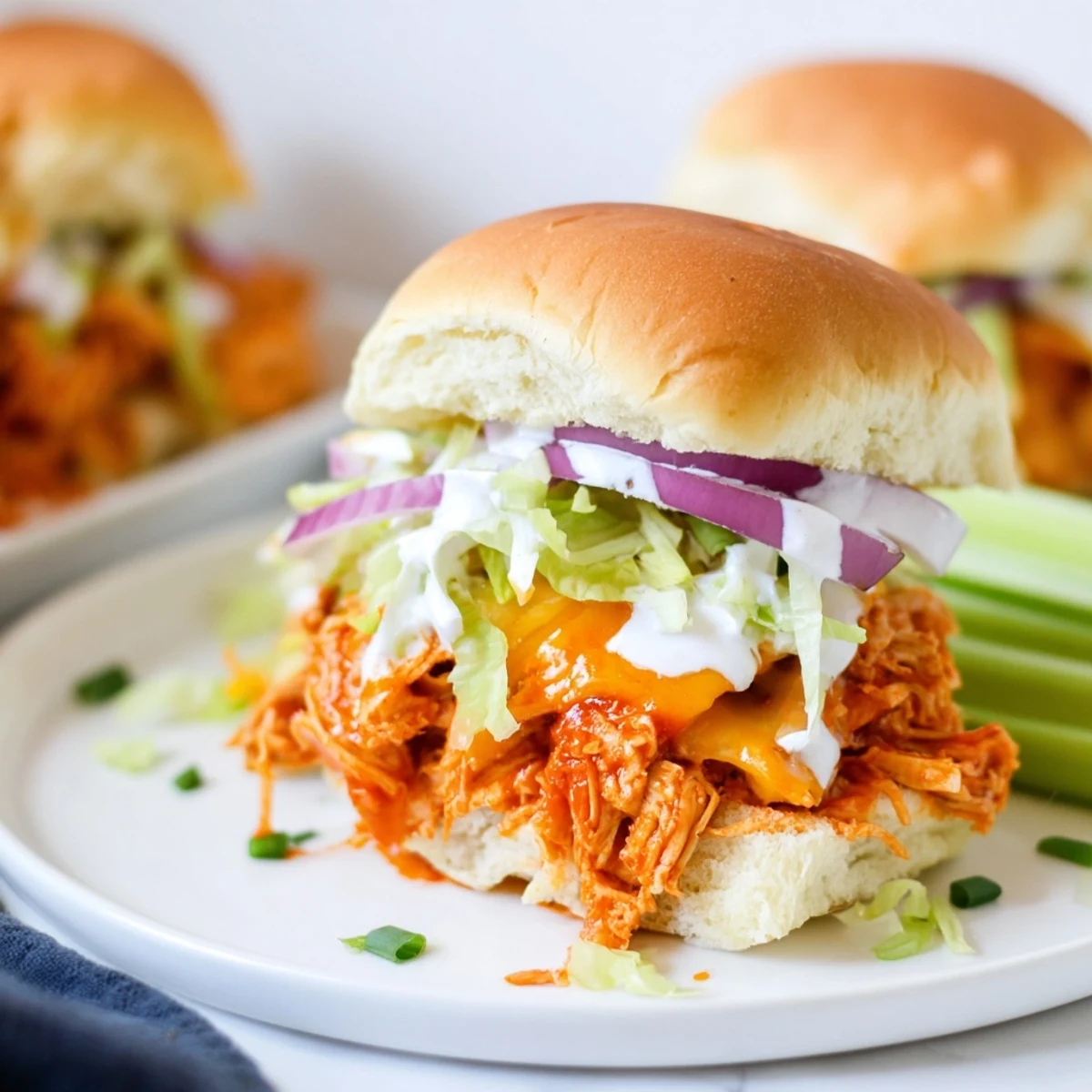 Freshly baked Buffalo Chicken Sliders with melted cheddar, celery, and red onion, drizzled with homemade ranch.