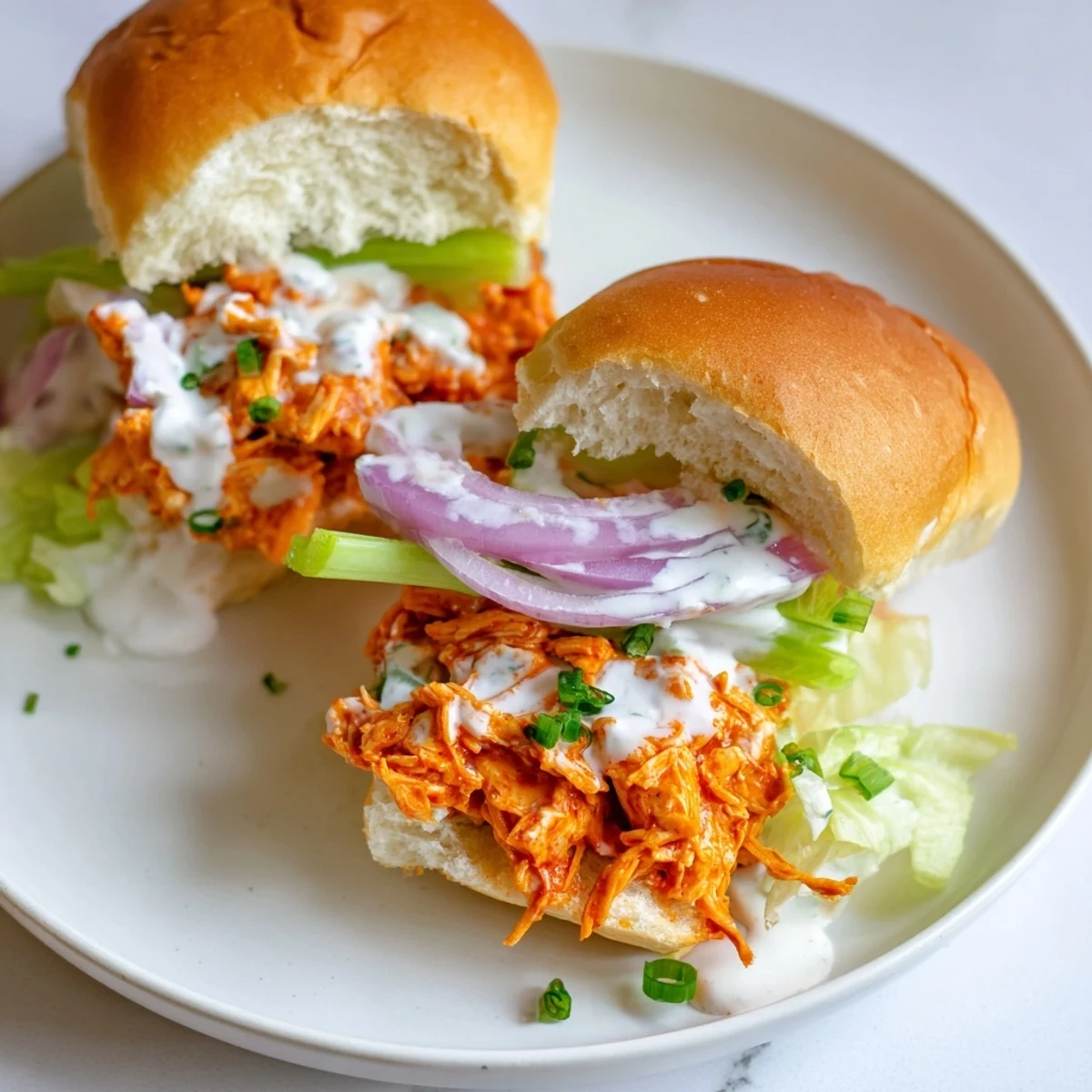 Tangy buffalo chicken sliders on golden buns, topped with shredded lettuce and rich ranch dressing for snacking.