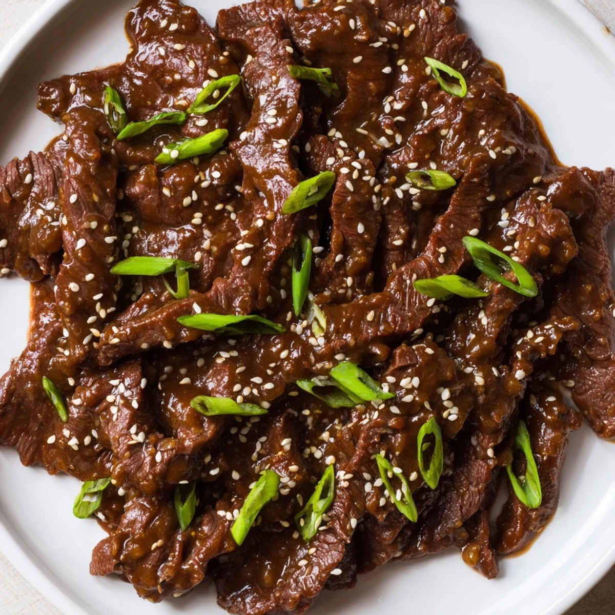 Steaming bowl of Ultimate Slow Cooker Mongolian Beef glazed with savory sauce and green onions.