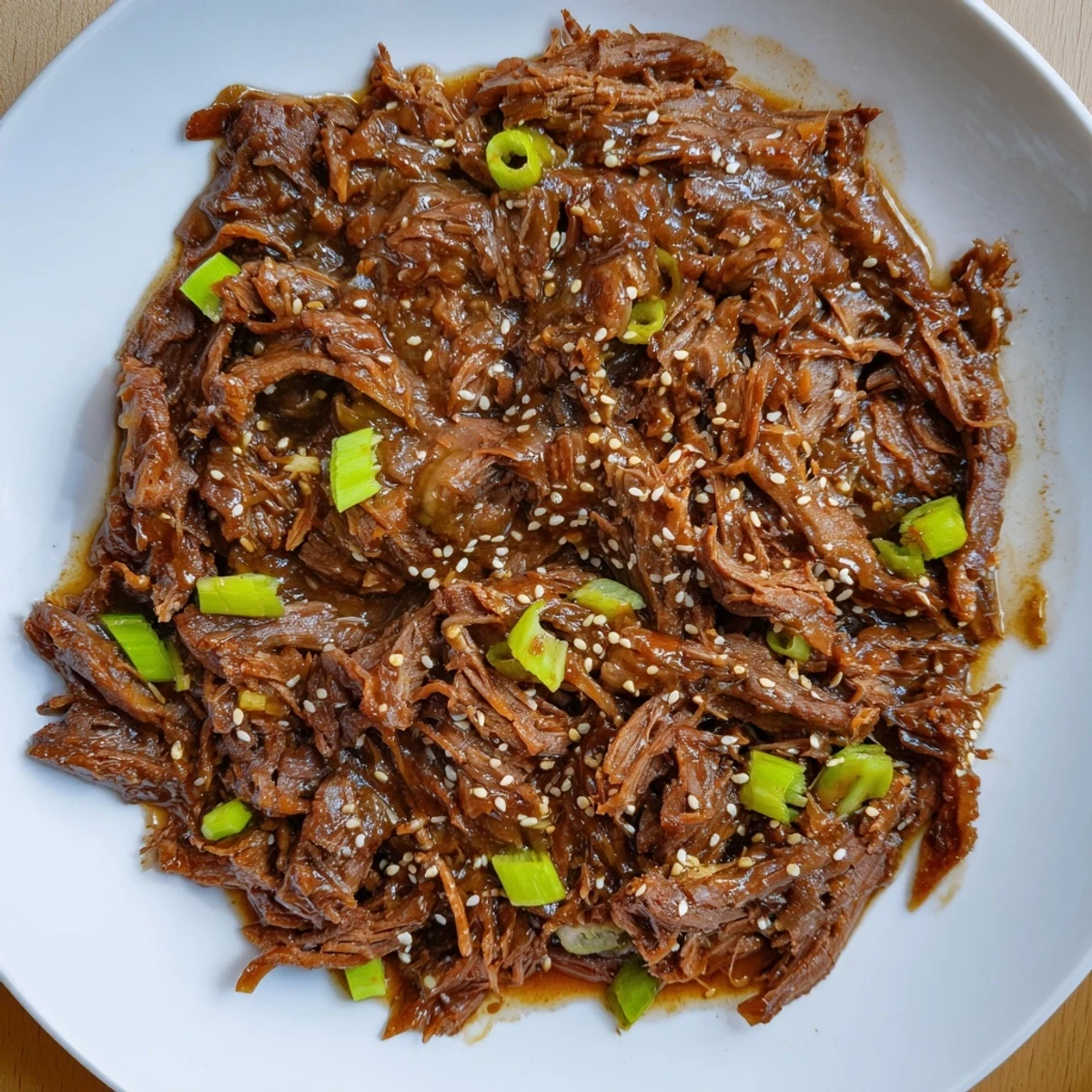 A close-up of tender shredded Crock Pot Korean Beef piled high on fluffy white rice with green onions and sesame seeds.