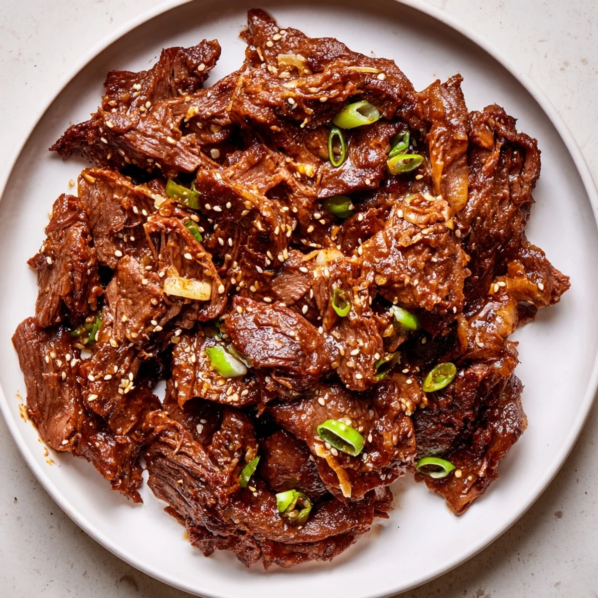 Slow cooker Korean beef recipe served in a black bowl, garnished with fresh scallions and a sprinkle of sesame seeds.