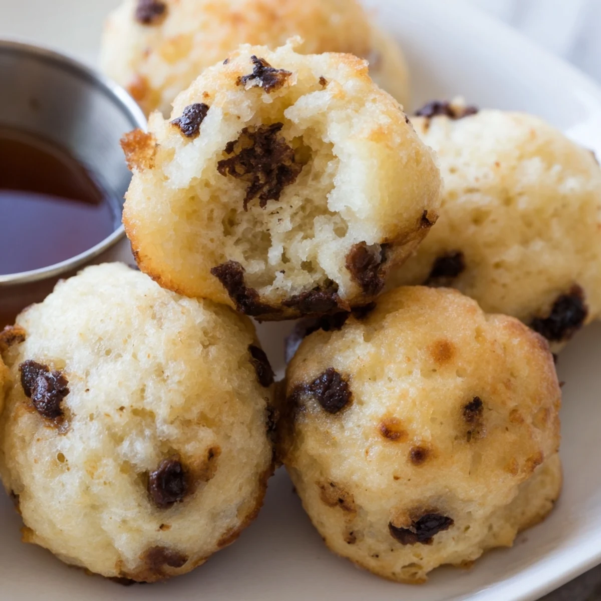 Golden-brown Pancake Poppers sprinkled with powdered sugar on a white plate, served with warm maple syrup and fresh berries.