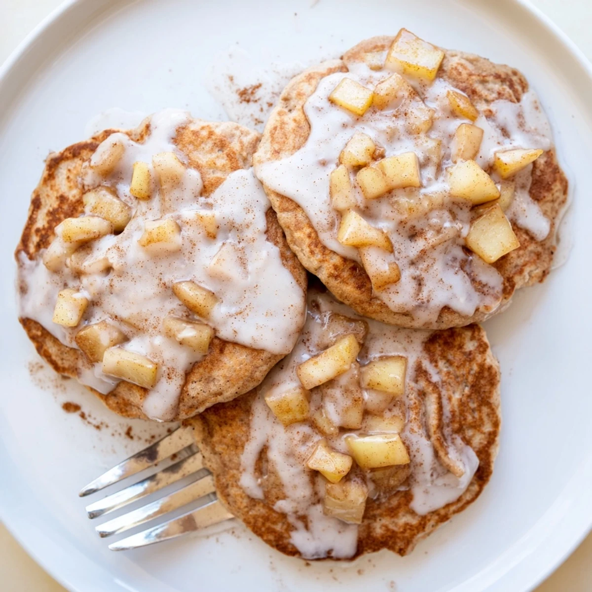 Apple Fritter Pancakes sizzling on a griddle, studded with tender cinnamon apples and fresh herbs nearby.