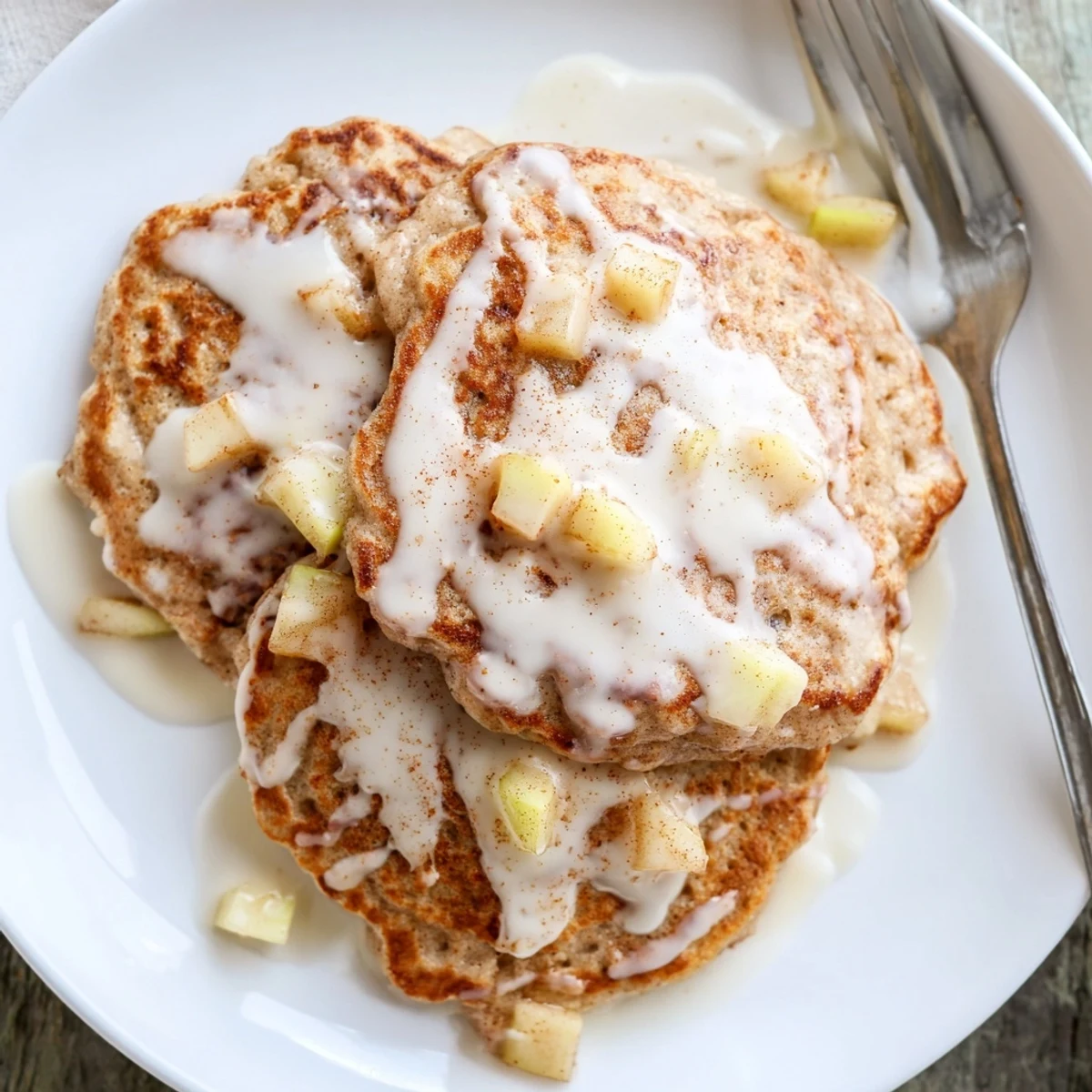 Golden Apple Fritter Pancakes topped with a sweet glaze, stacked high on a white plate, ready for a cozy breakfast.