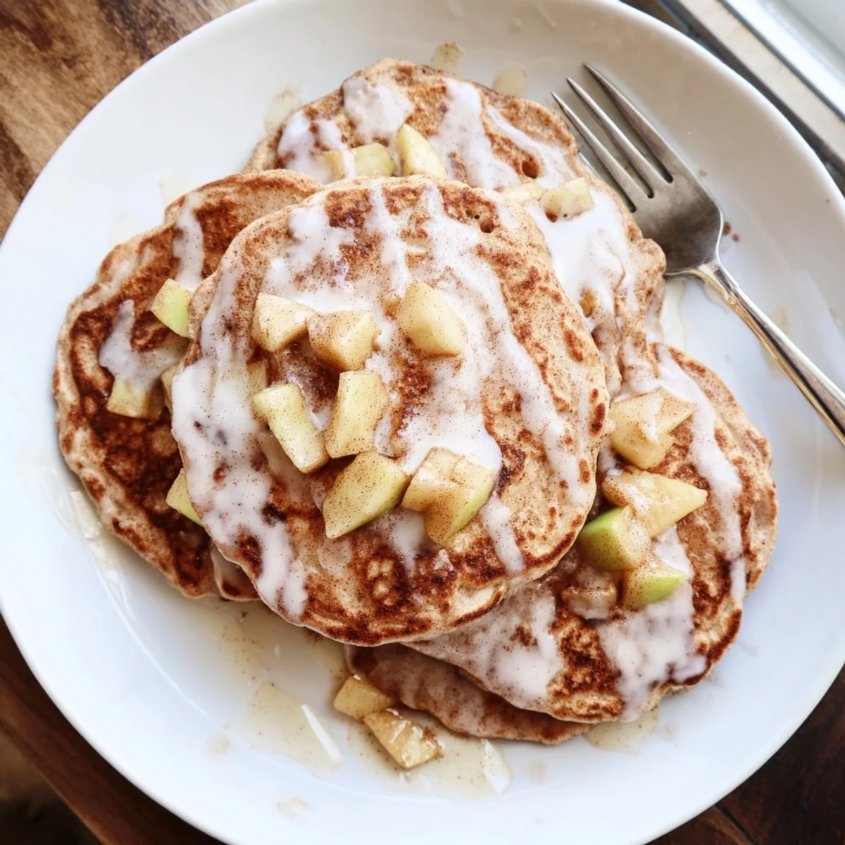 Warm Apple Fritter Pancakes drizzled with vanilla glaze, served with maple syrup and a pat of butter.
