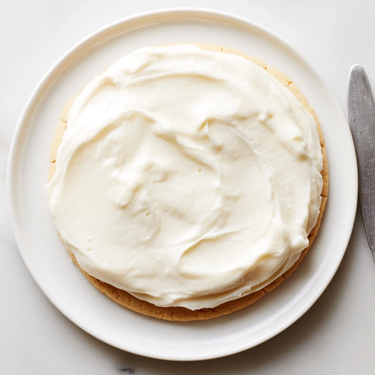 Easy Sugar Cookie Frosting in a white bowl with a whisk, showing a creamy texture ready to color.