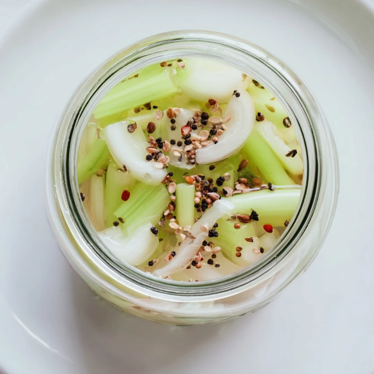Bright Quick Pickled Celery glistening in a jar, with tangy brine and red pepper flakes for a vibrant garnish.