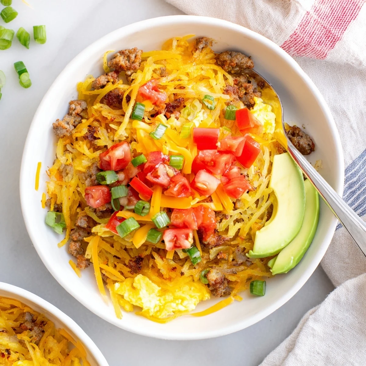 Crispy golden hash browns topped with fluffy scrambled eggs and savory sausage in a Hash Brown Breakfast Bowl with fresh avocado.