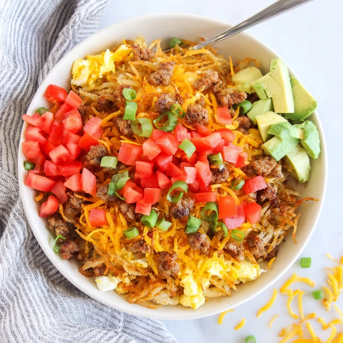 A delicious Hash Brown Breakfast Bowl featuring crumbled sausage, creamy avocado slices, and a drizzle of hot sauce for extra kick.