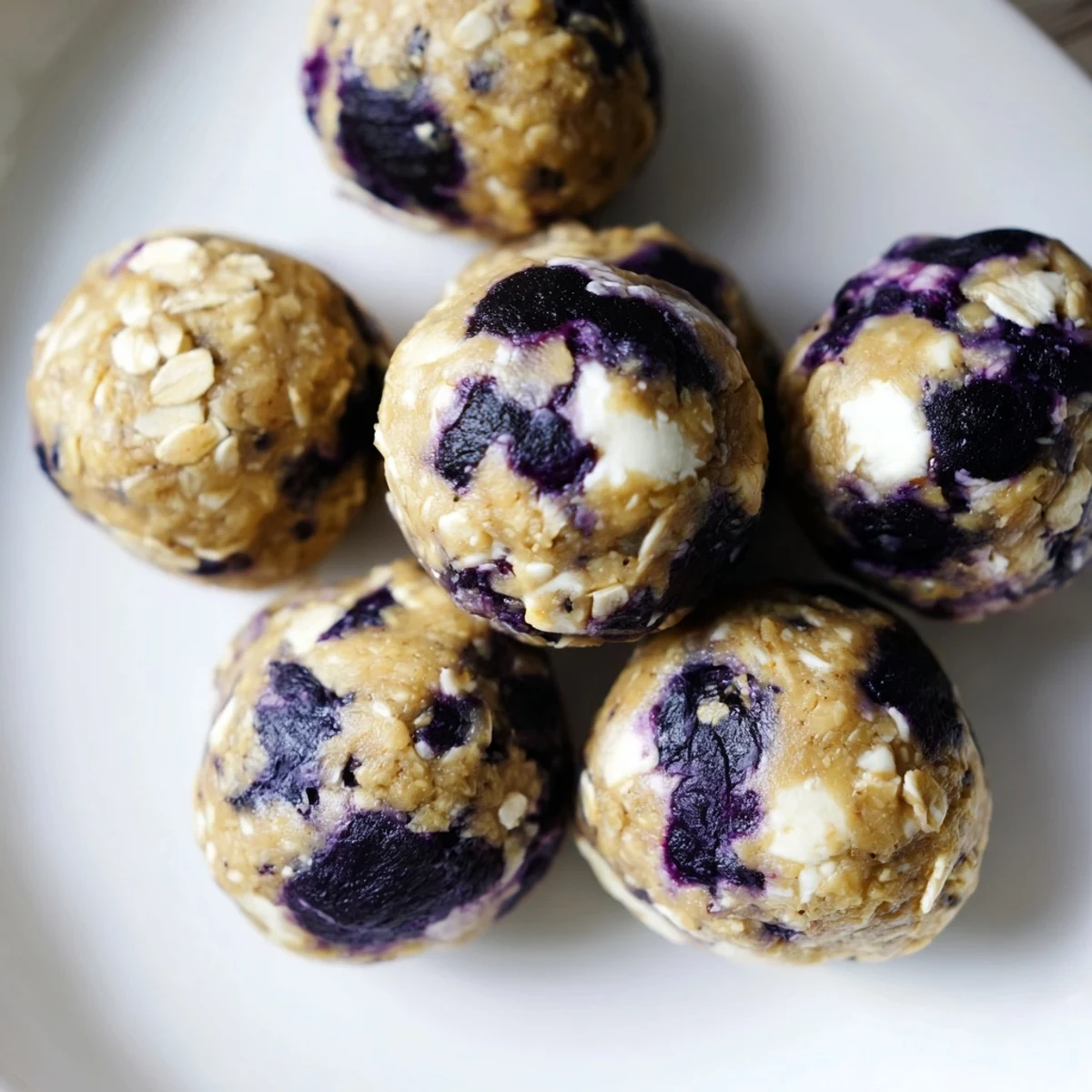 A close-up of Blueberry Cheesecake Protein Bites highlights soft oats, tangy cream cheese, and bursts of sweet dried blueberries.