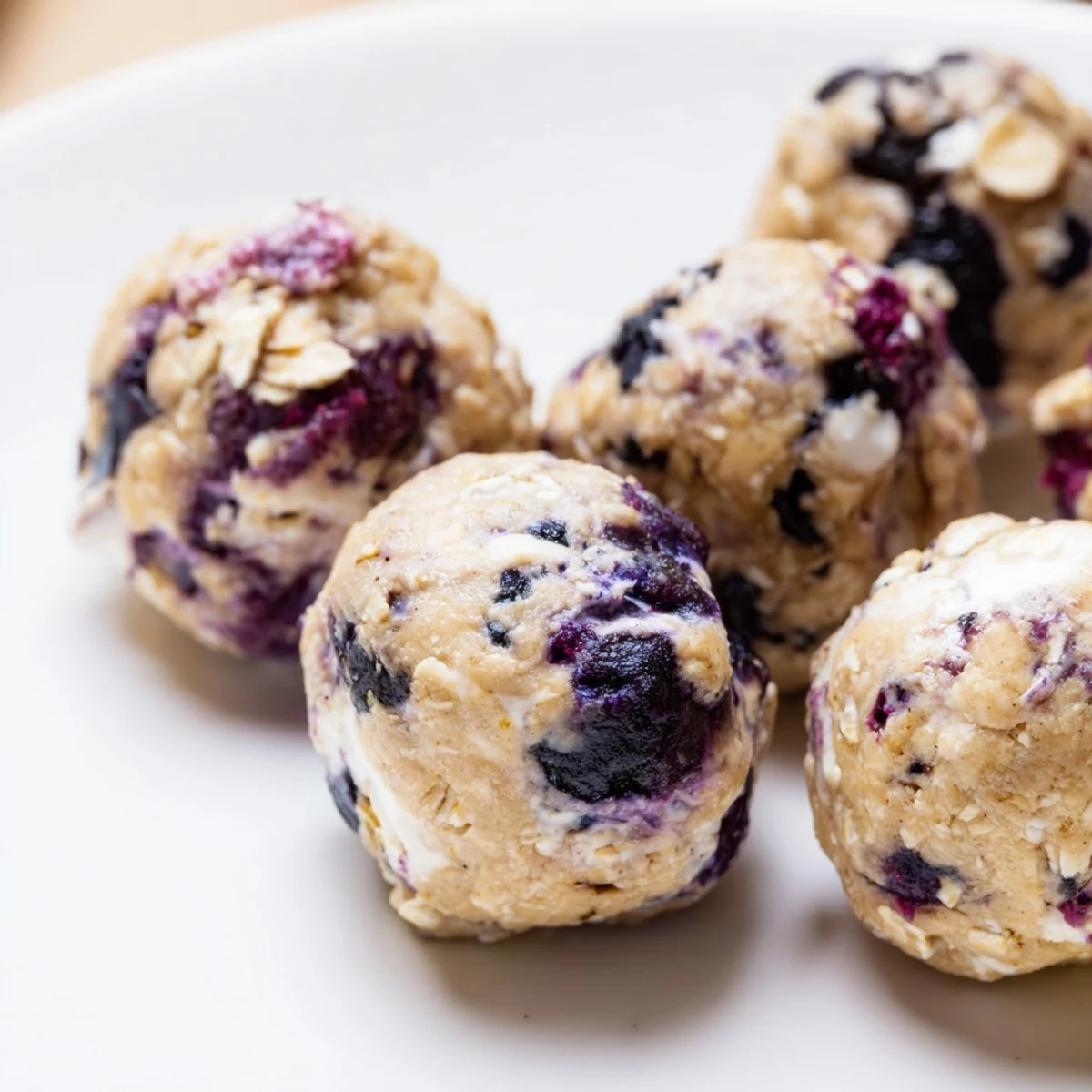 On a rustic wooden board, Blueberry Cheesecake Protein Bites are served alongside a glass of cold milk for dipping.