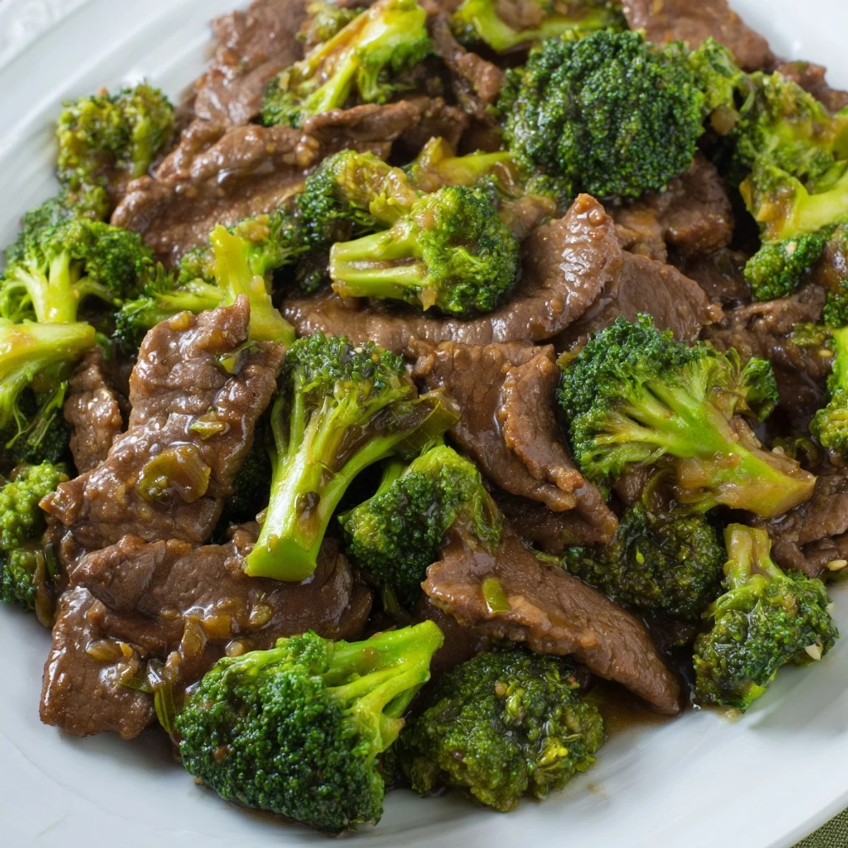 Homemade better than takeout beef with broccoli plated next to chopsticks and a small dipping sauce.