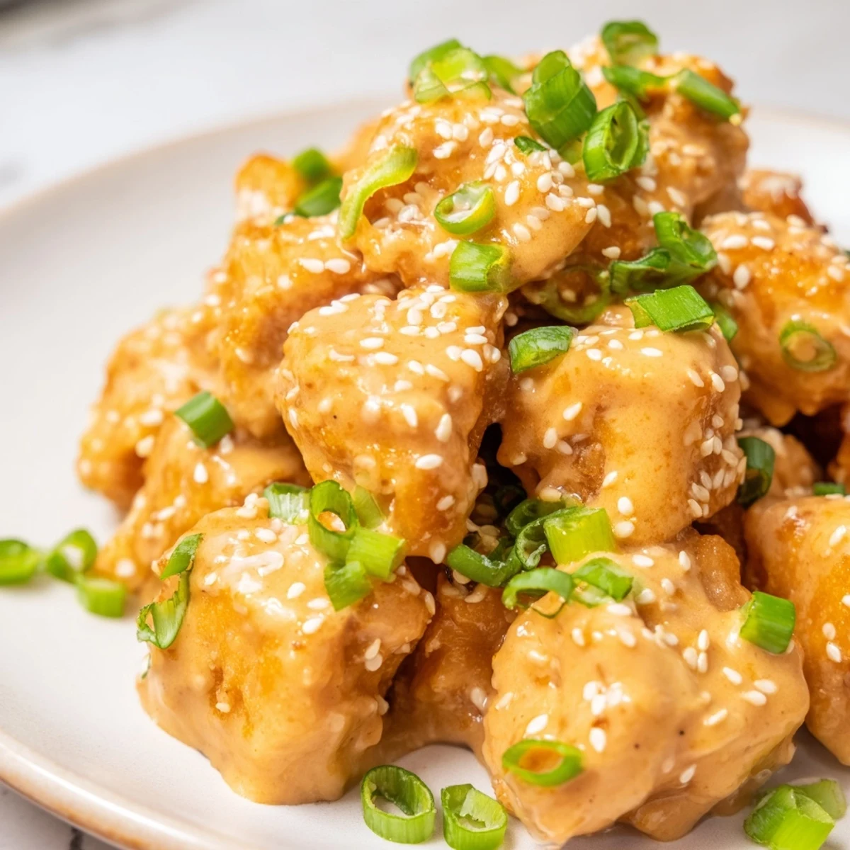 Close-up of Bang Bang Salmon Bites tossed in Bang Bang sauce, garnished with green onions on skillet.