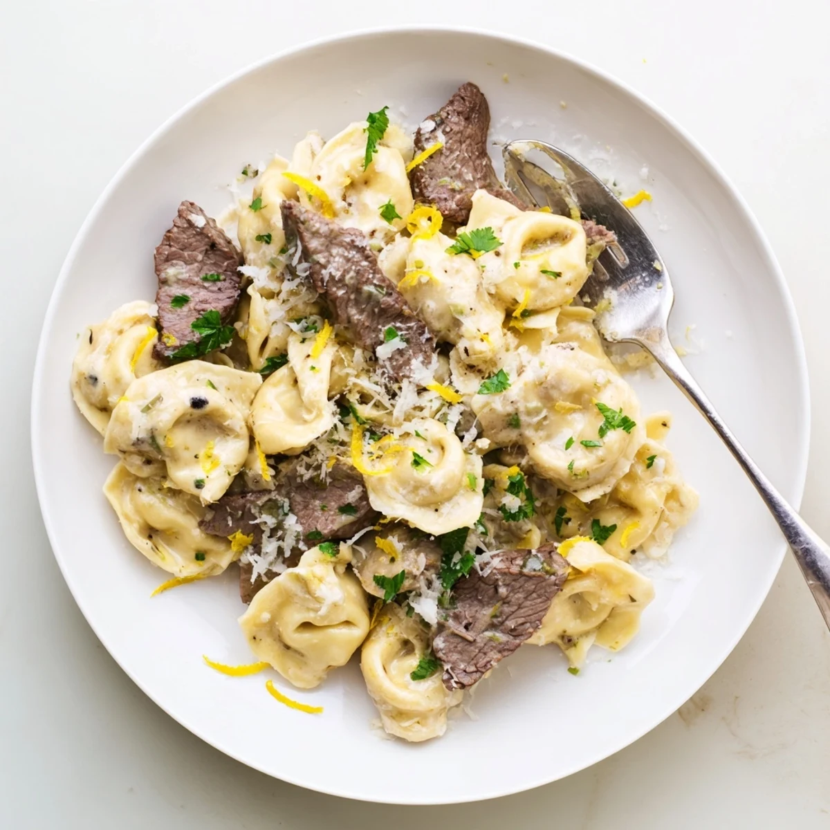 Golden brown sliced steak nestled among cheese tortellini in a rich creamy garlic parmesan sauce