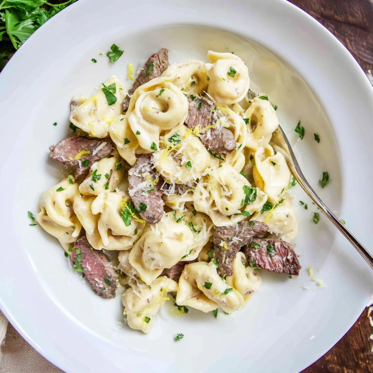 Plated pasta dish featuring seared beef strips and tortellini coated in a smooth white cream sauce