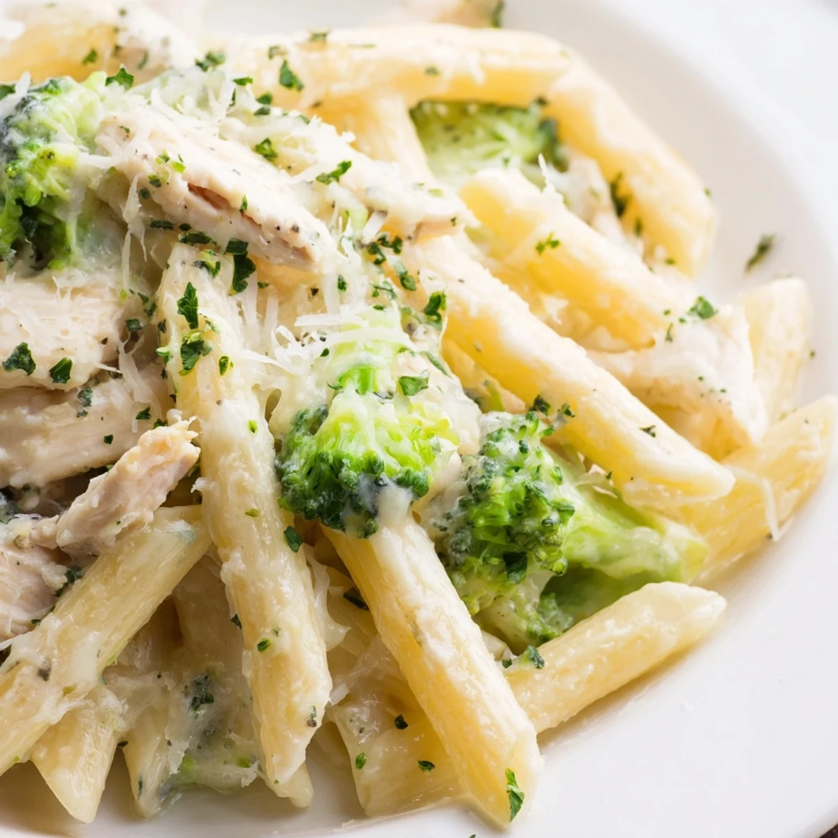 Creamy rotisserie chicken broccoli pasta in a white bowl topped with fresh parsley and Parmesan cheese