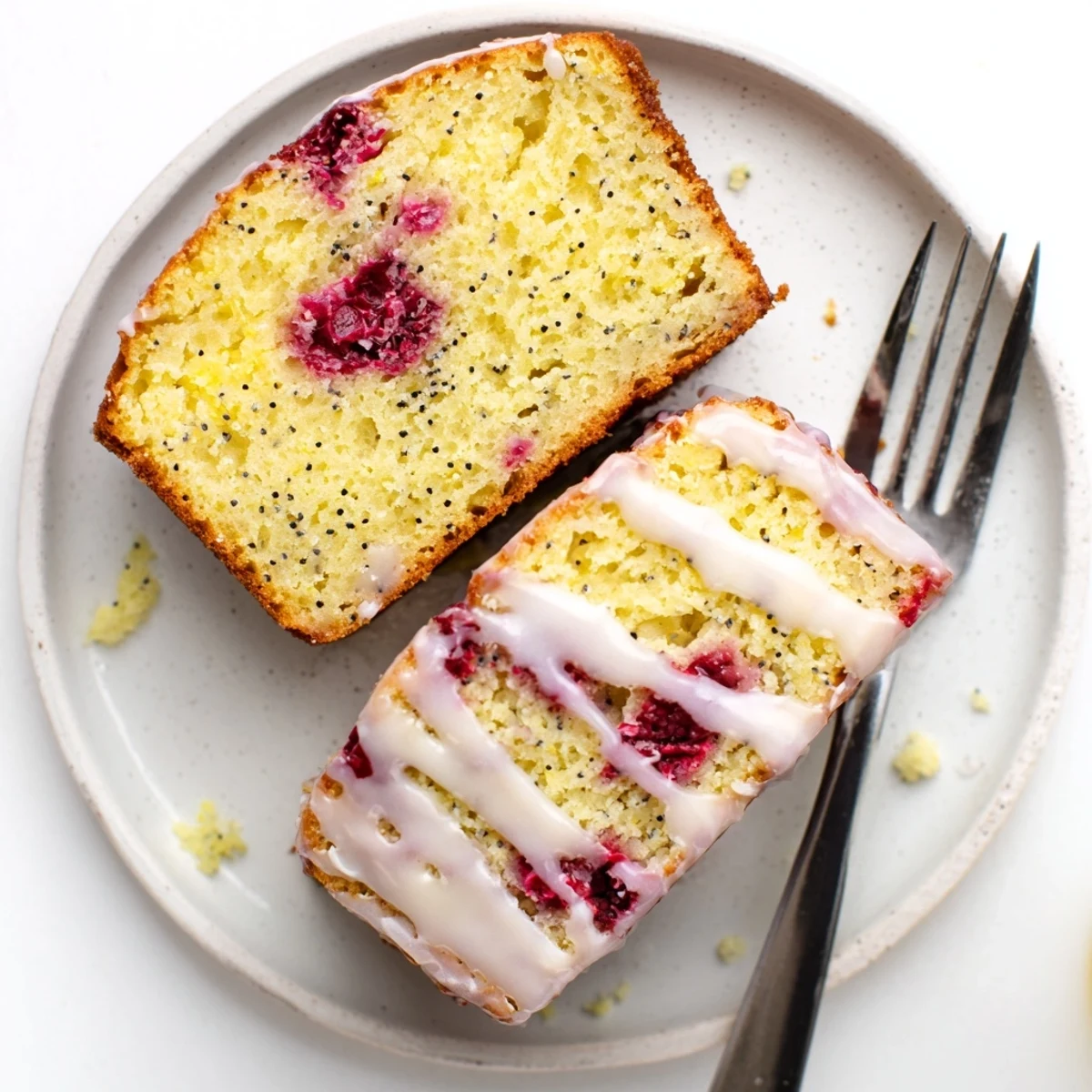Golden raspberry lemon poppyseed loaf cake drizzled with white lemon glaze on a white plate