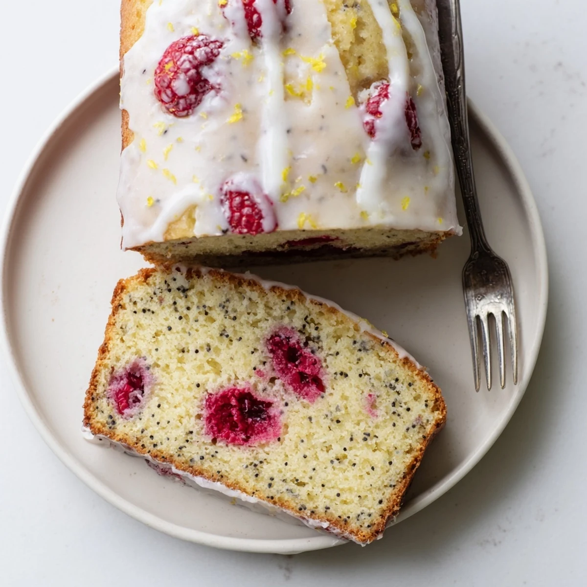 Moist lemon poppyseed loaf cake studded with fresh red raspberries sliced on a wooden board
