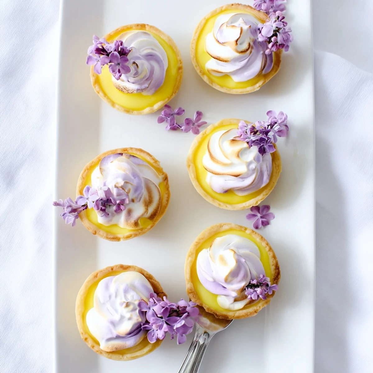 Crisp tart shell filled with bright lemon curd and fluffy floral meringue garnished with edible flowers