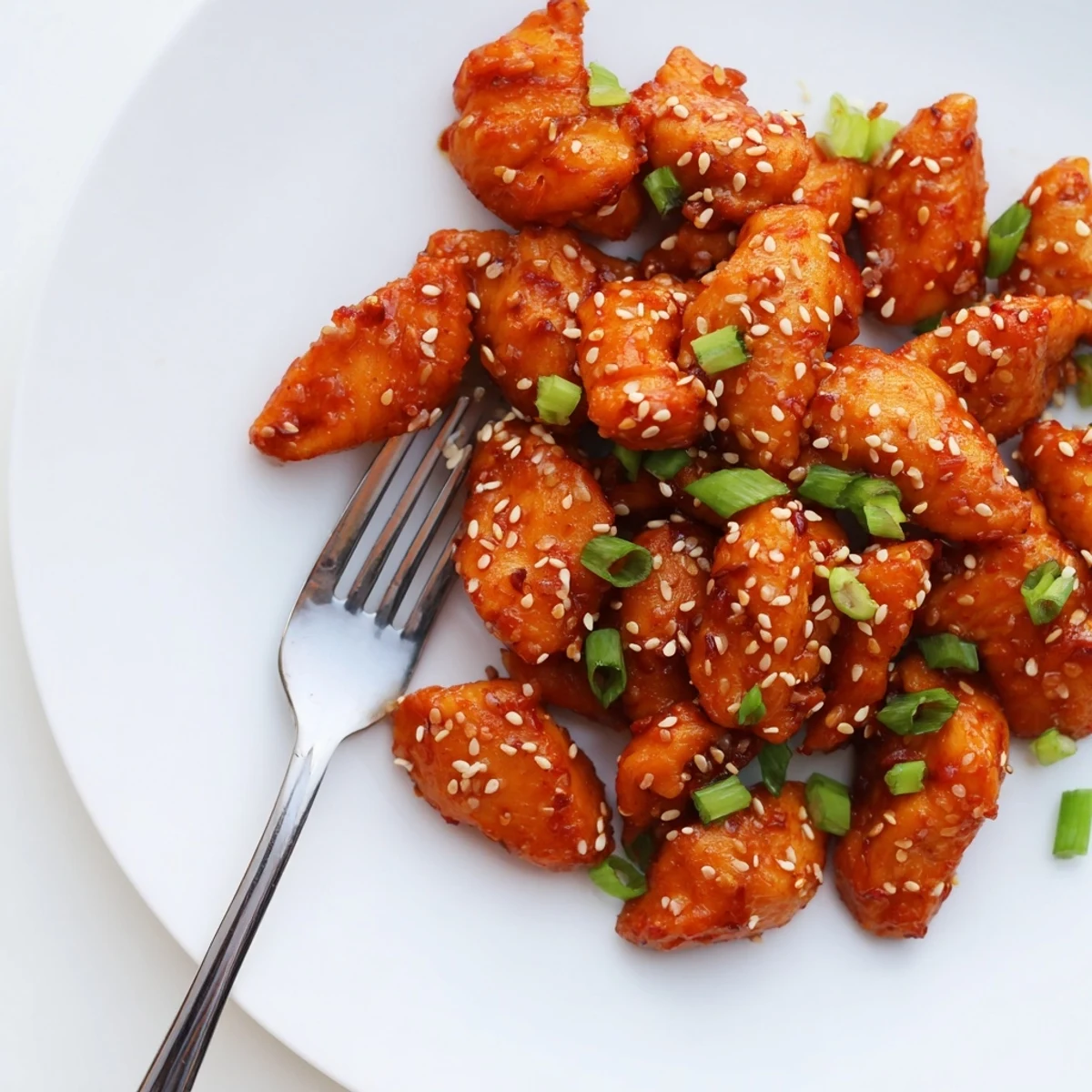 Glossy red sweet chili chicken garnished with green onions and sesame seeds over white rice