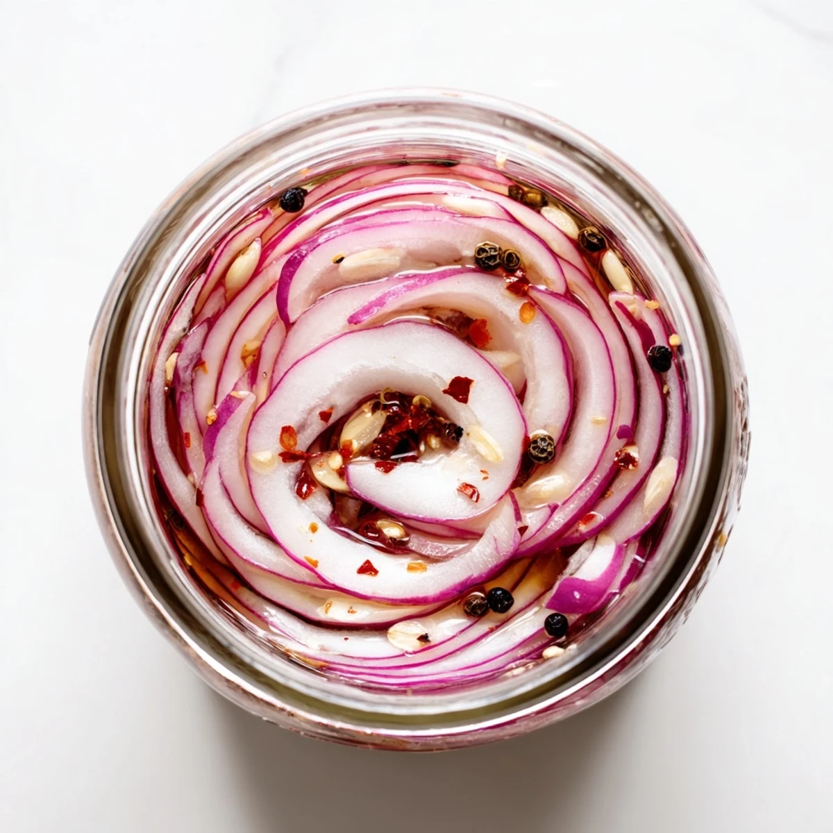 Mason jar displaying thinly sliced red onions pickled in hot honey with garlic and spices