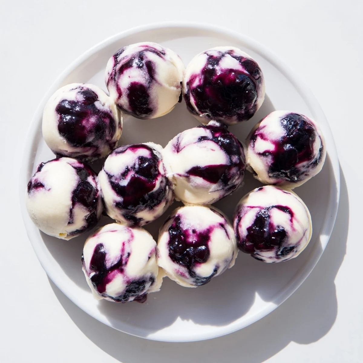 Frozen blueberry swirl yogurt bites on a white plate with a toothpick nearby showing the marble pattern of berry and yogurt layers