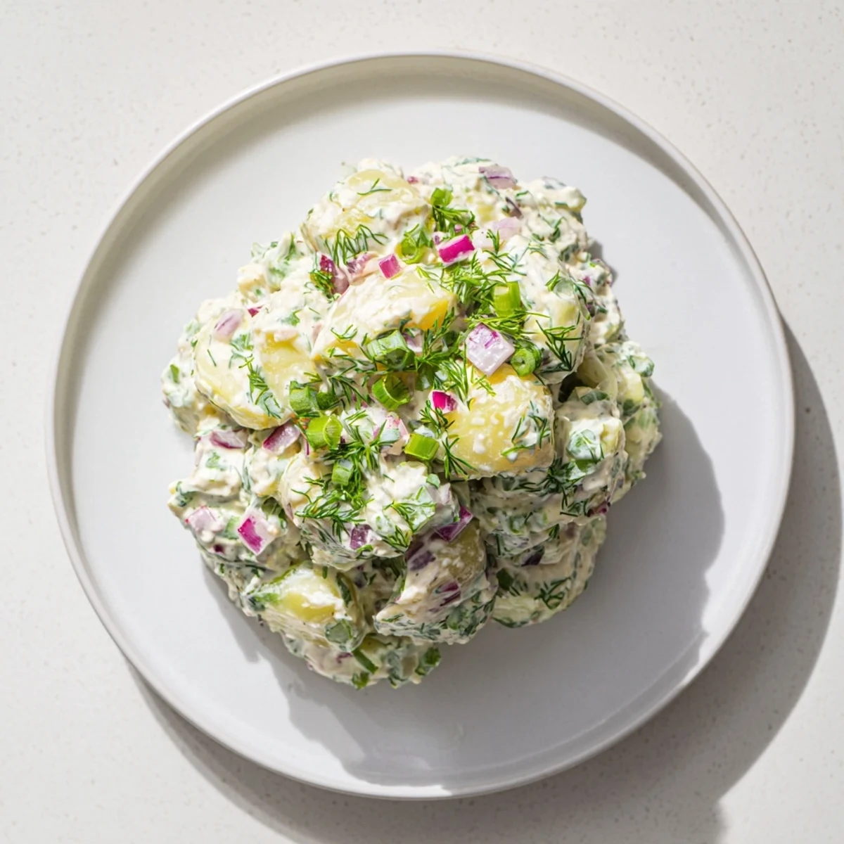 Vibrant bowl of Greek yogurt potato salad tossed with colorful vegetables and garnished with fresh green herbs