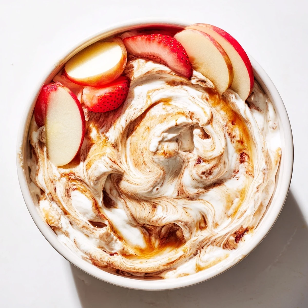 Creamy Greek yogurt cinnamon roll dip swirled with cinnamon and served with fresh apple slices, strawberries, and grapes