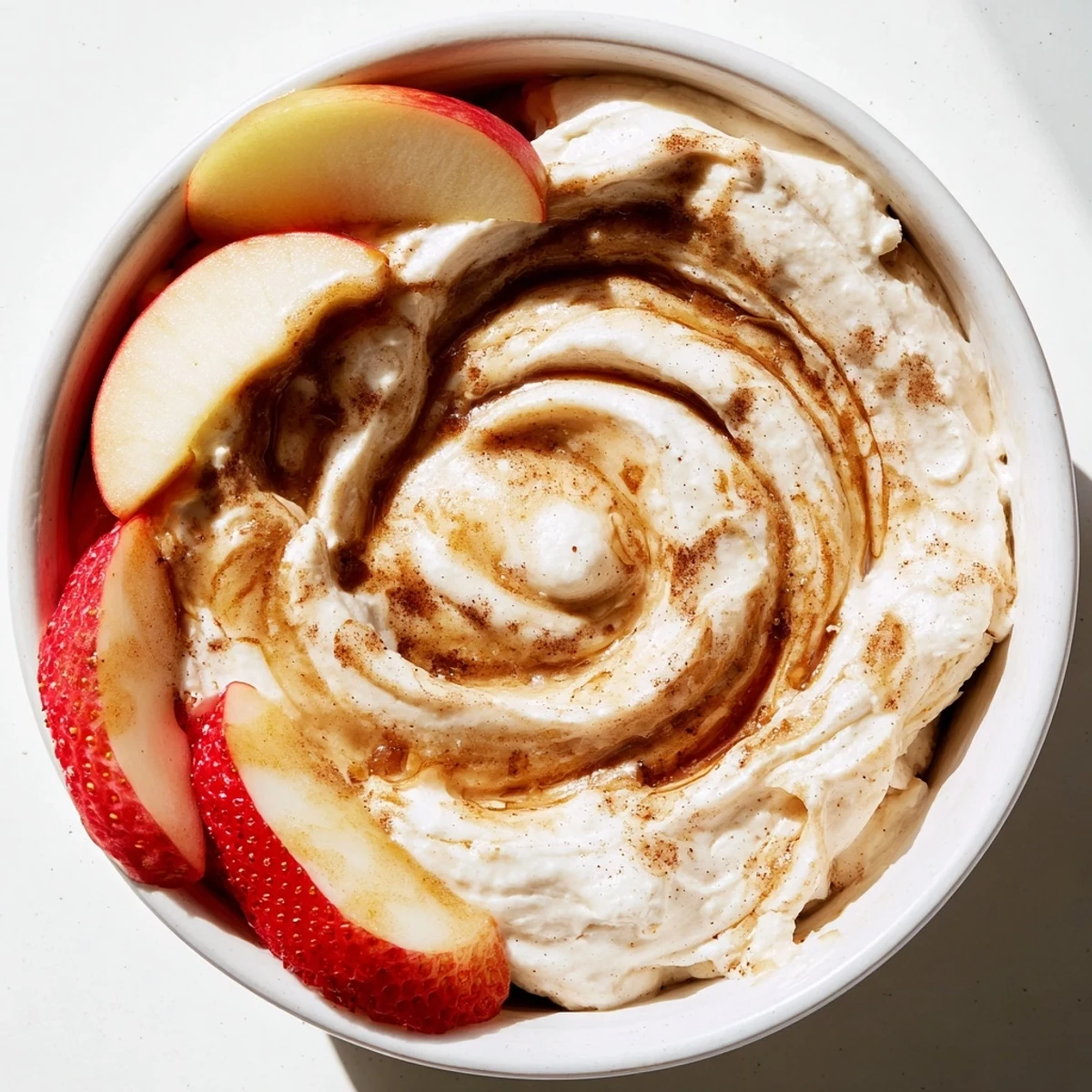 Healthy Greek yogurt cinnamon roll dip in a white bowl surrounded by freshly sliced pears, bananas, and orange segments