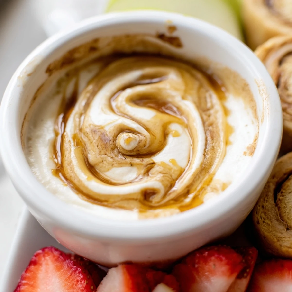 Protein-packed cinnamon roll dip featuring Greek yogurt cream cheese base topped with maple cinnamon swirl and colorful fruit dippers