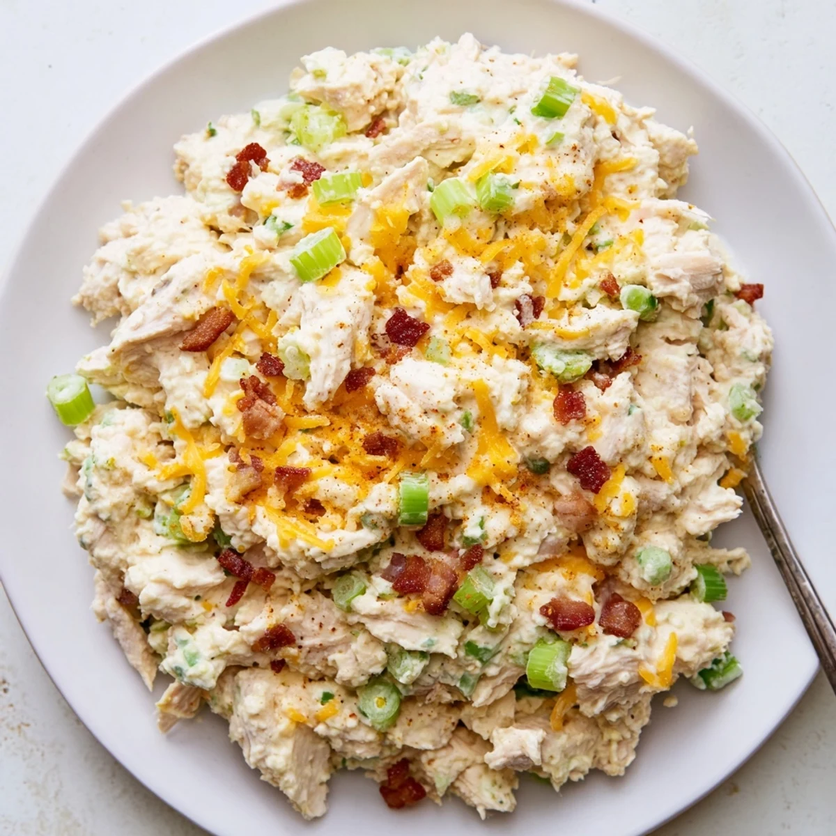Creamy jalapeno popper keto chicken salad served in a white bowl topped with crispy bacon bits