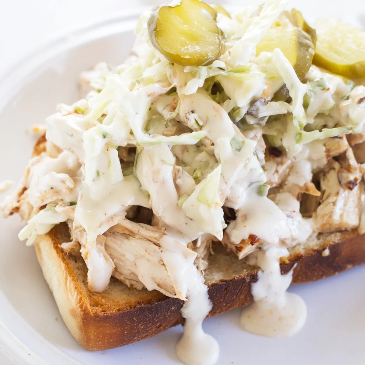 Golden Alabama BBQ chicken chopped sandwich topped with creamy white sauce and crisp slaw on toasted bun