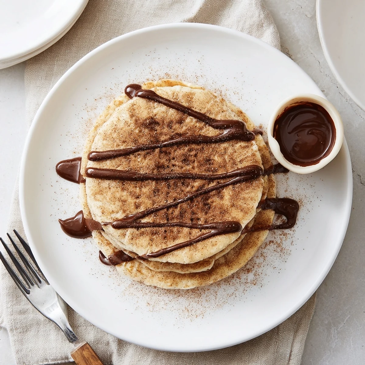 Fluffy Spanish churro pancakes stacked high with glossy chocolate sauce drizzled on top