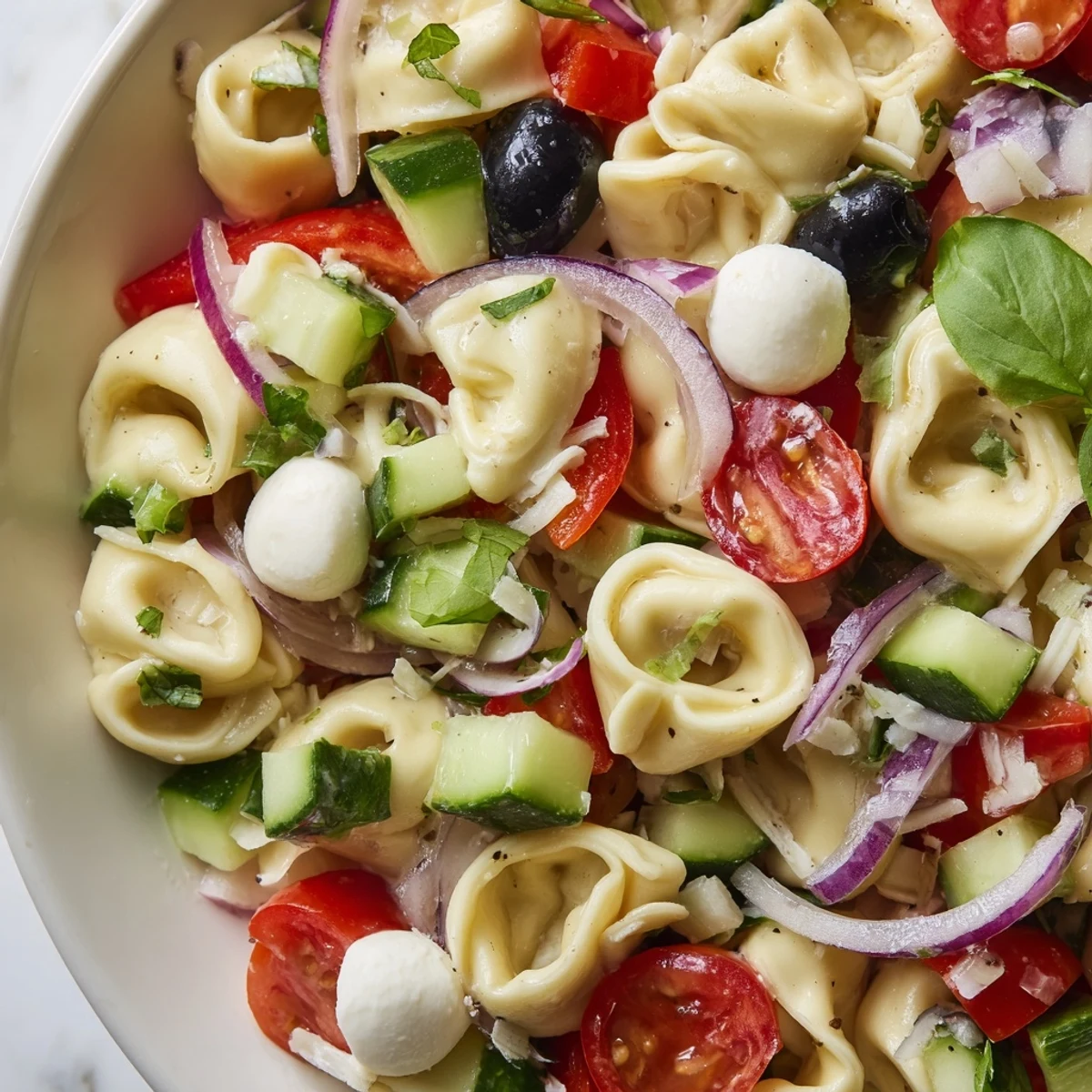 Creamy cheese tortellini salad loaded with crisp vegetables and fresh basil in a bowl