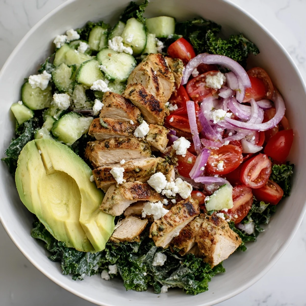 Golden sliced chicken rests atop massaged kale with vibrant cherry tomatoes and creamy avocado slices in a marinated kale and chicken bowl