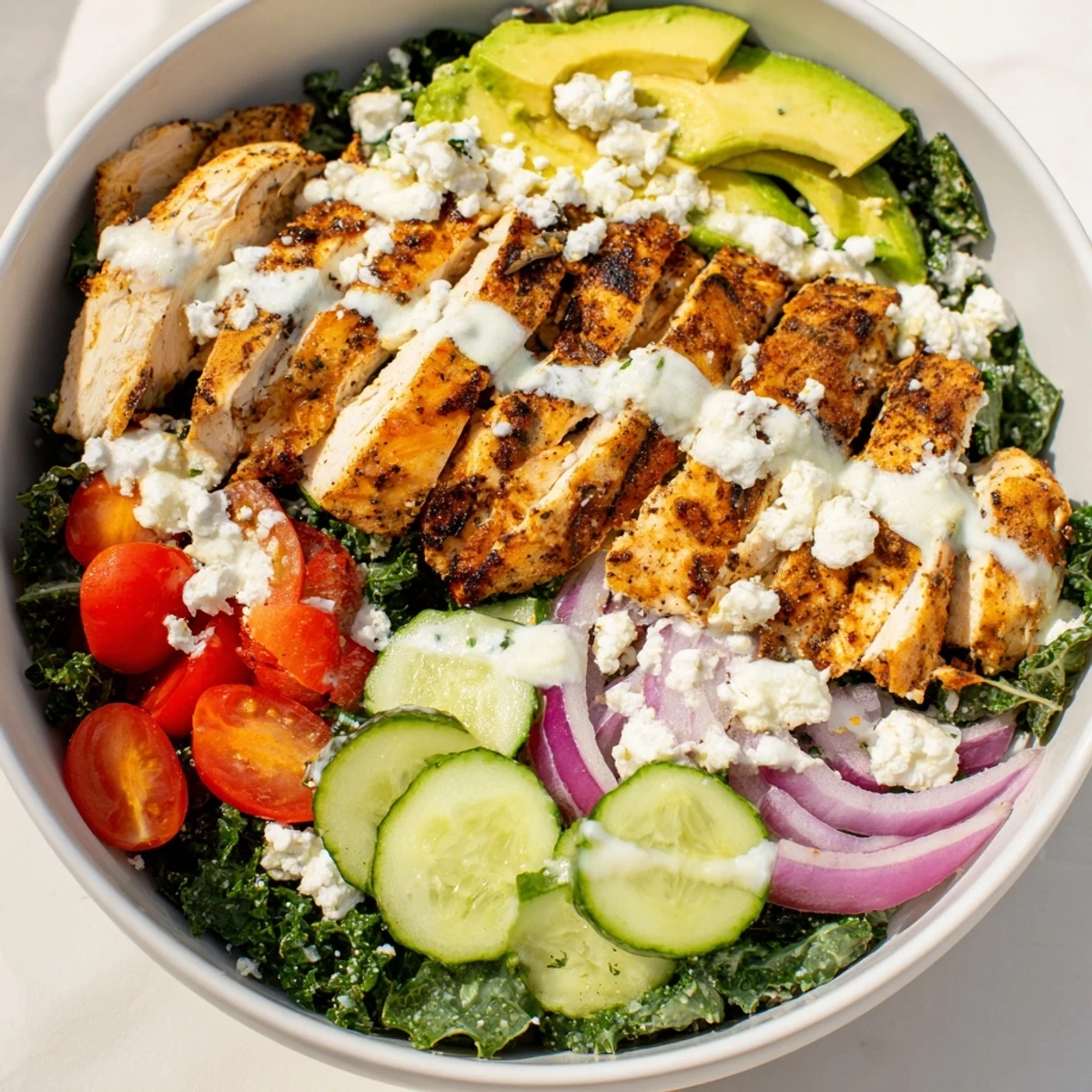 Wholesome lunch bowl displaying tender spiced chicken alongside bright green kale, red onions, and halved cherry tomatoes with tangy yogurt dressing