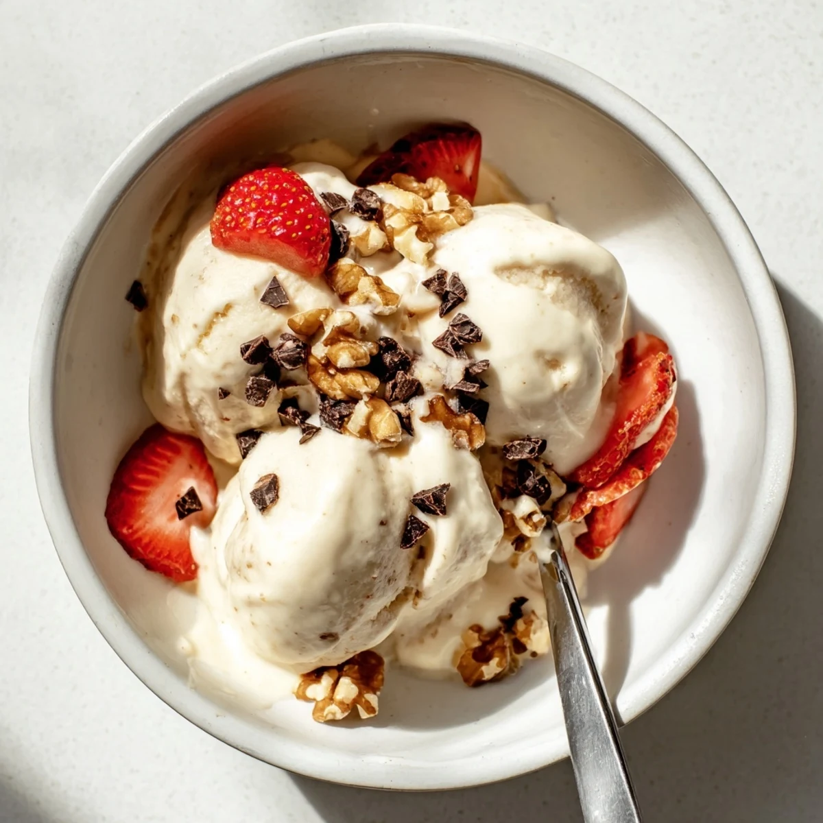 Creamy banana nice cream scooped into bowls topped with fresh berries and chopped nuts