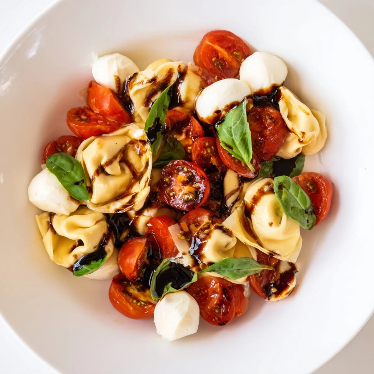 Vibrant summer Tortellini Caprese Salad in a white bowl topped with torn basil and glossy balsamic dressing
